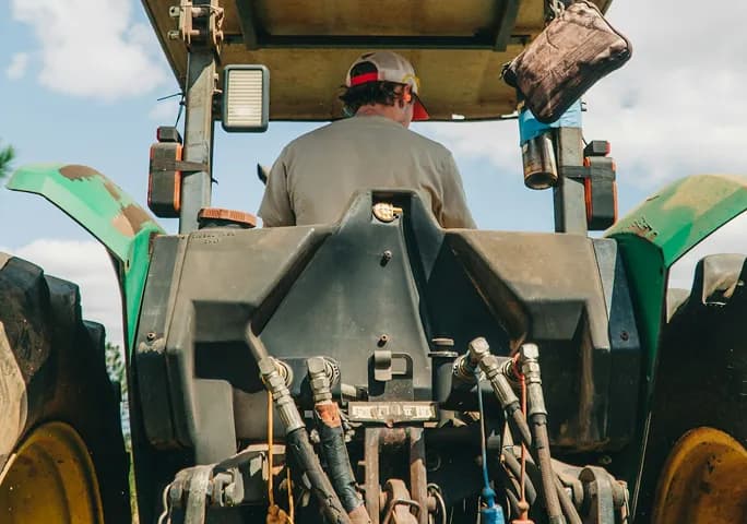 A tractor driver working a field, seen from behind