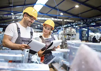 Two production workers in hard hats checking paperwork on the factory floor