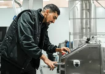 A machine operator adjusting the controls of a stainless steel processing machine