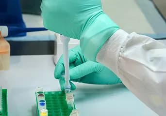 Gloved hands pipetting samples into a rack of test tubes