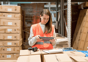 A pick packer checking an order on a tablet beside stacked cartons