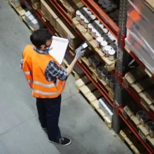 Pick packer in a warehouse, counting stock and marking it on a clipboard